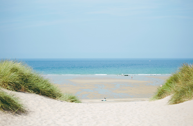 Looking through the sand dunes at the white sands and blue seas at Holywell Bay near Newquay