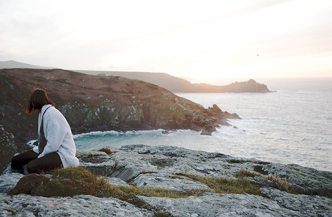 Someone sitting on a rock looking out across the coastline towards Zennor