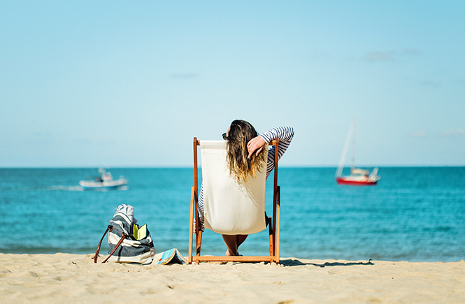 A woman sitting in a deckchair looking out to sea on a sunny day