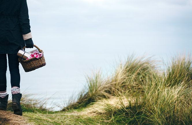 Someone carrying a basket with a thermos and blankets for a winter picnic in Cornwall