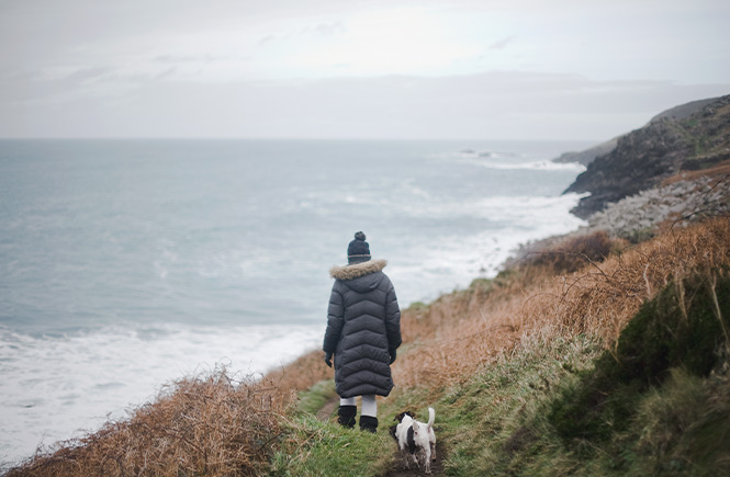 Someone in a big coat walking their dog along the Cornish cliffs in winter