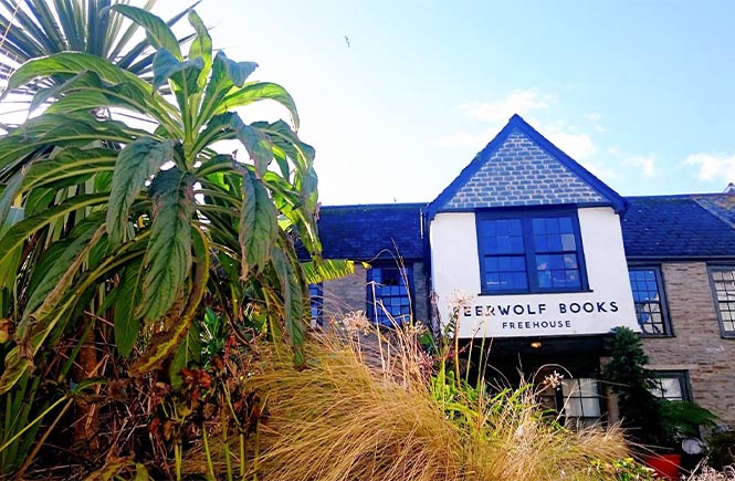 Looking across some plants at the traditional exterior of Beerwolf Books Freehouse in Falmouth