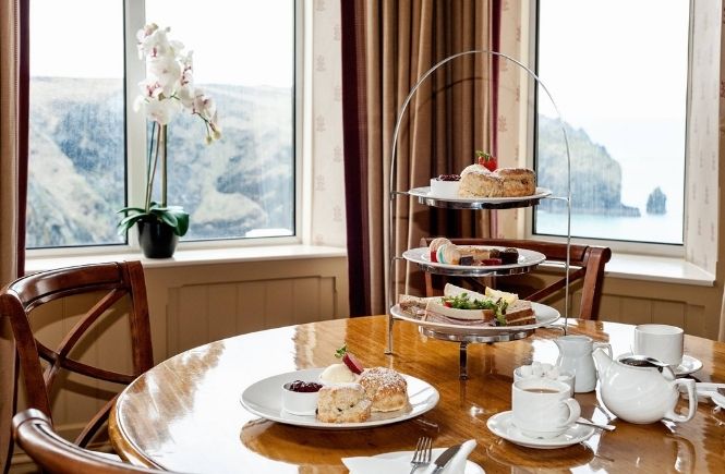 An afternoon tea in front of a window looking out over the cliffs and sea at Mullion Cove Hotel