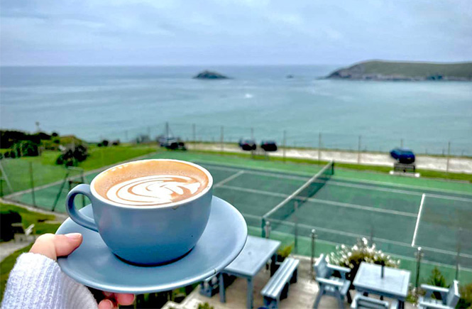 Someone holding a coffee while looking out over the tennis courts and beach in the distance