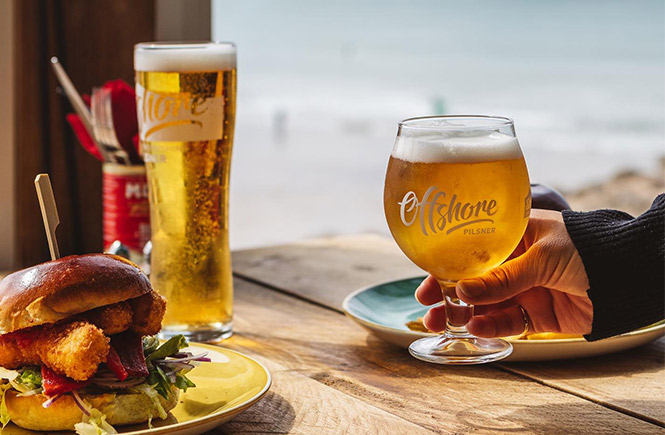 A fish burger and beer being enjoyed at the Great Western Surf Cafe with the beach behind