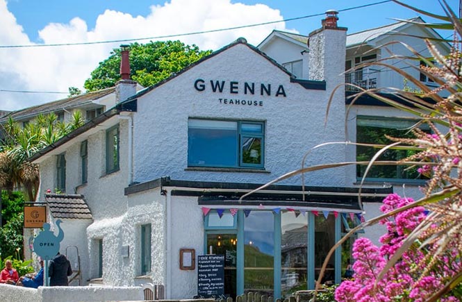 The quaint exterior of Gwenna Teahouse surrounded by trees and flowers