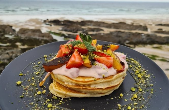 A plate of pancakes topped with strawberries in front of the sea at Sea Spray