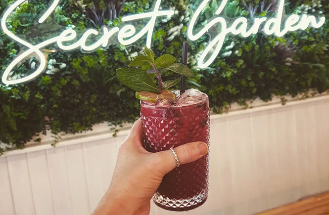 Someone holding a cocktail up in front of the Secret Garden sign