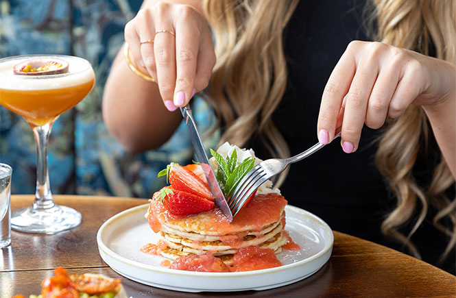 Someone eating a stack of pancakes with a cocktail during a bottomless brunch at the Slug & Lettuce in Newquay