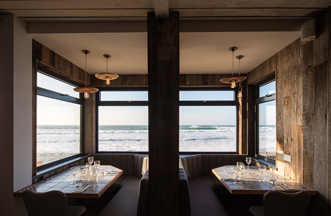 Two well-positioned tables at The Beach Hut overlook the beach and waves at Watergate Bay