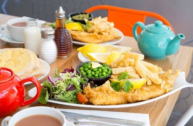 Plates full of fish and chips with colourful teapots and chairs at Fraser's Fish and Chips in Penzance