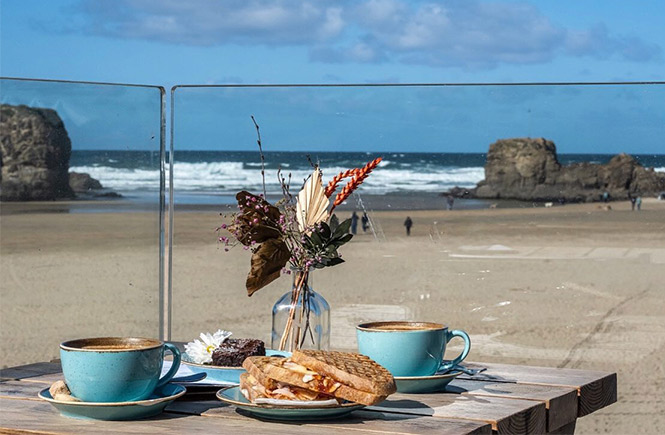 A table full of fresh coffee and sandwiches at Alcatraz with Perranporth beach and sea behind