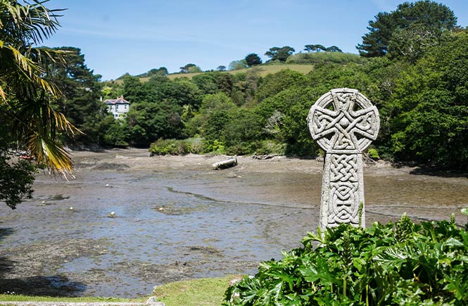 An ancient Celtic cross at St Just in Roseland Church with the estuary behind