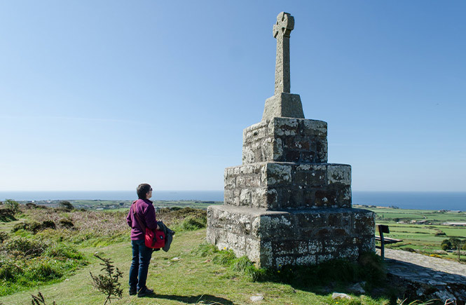 Someone looking at the war memorial on top of Tregonning Hill with the Cornish countryside stretching out behind