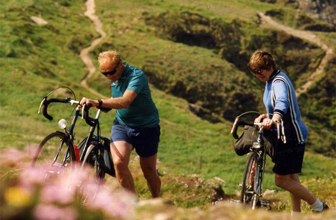 A couple pushing their bikes up a coastal path at Cape Cornwall while off-roading