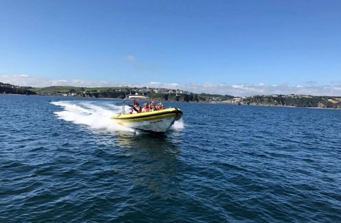 A boat full of people speeding across the water with Mevagissey Rib Rides