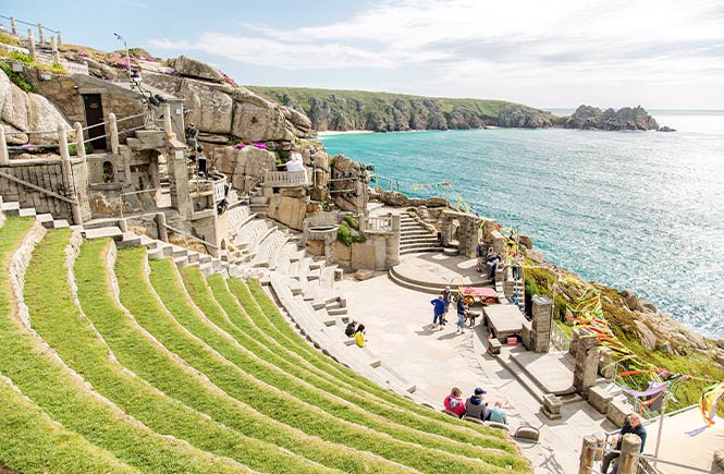 Looking down the grass-topped seats at the Minack Theatre with the ocean and coast behind