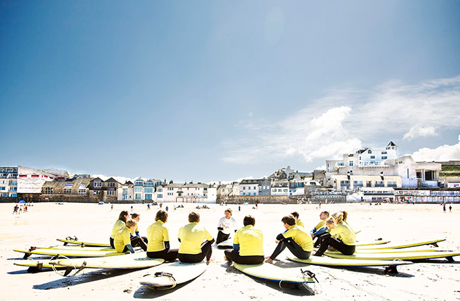 A group of people sit in a circle with their surfboards on Porthmeor beach for a lesson with St Ives Surf School
