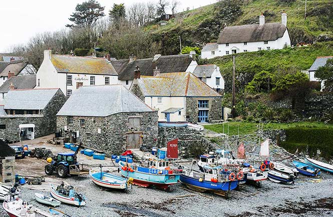 The pebbly beach at Cadgwith with boats lying on the shore of the harbour and cottages behind