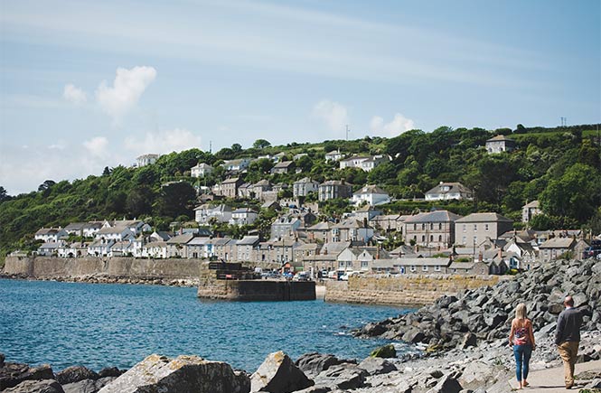 Two people walking alongside the rocks towards Mousehole harbour and village