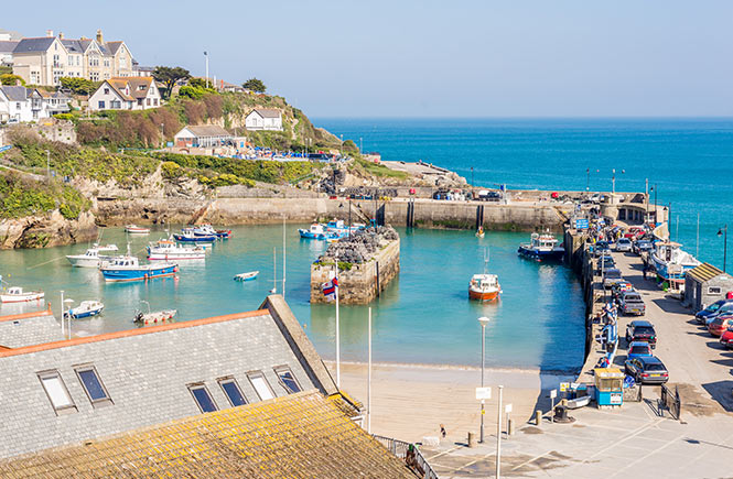 Looking down at the turquoise waters of Newquay harbour where boats bob and people walk on the beach