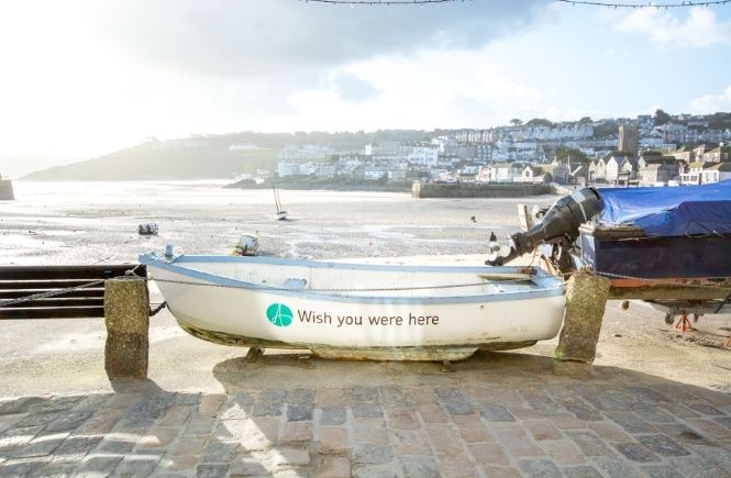 A boat with wish you were here on in St Ives with the harbour behind