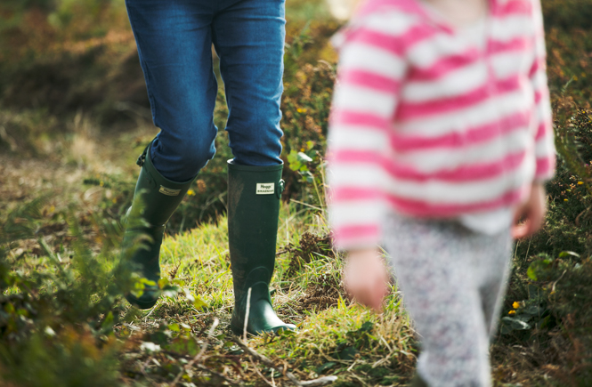 A parent and child walking through vegetation in wellies