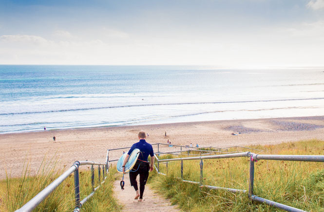 Surfer walking down the steps to Praa Sands Beach