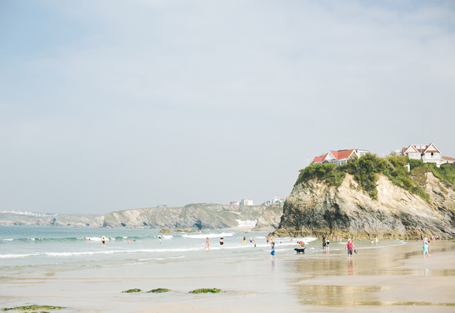 People paddling in the water at Towan beach in front of the cliff with houses on