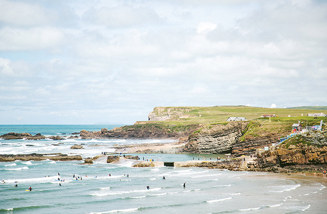 People surfing at Bude beach with the cliffs in the background