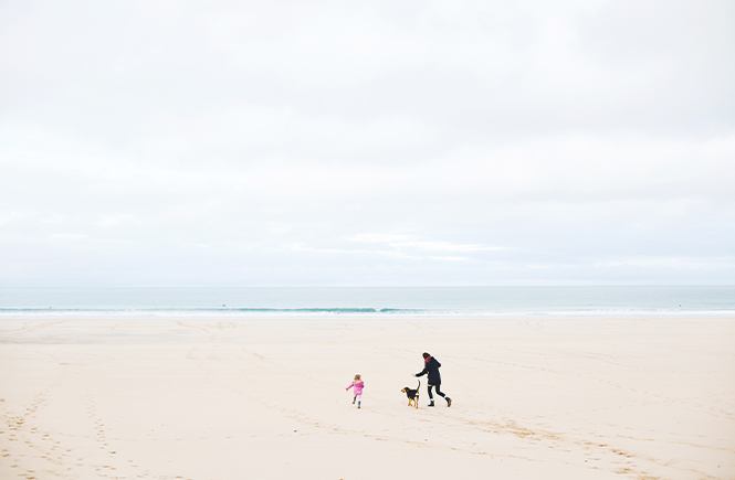A parent, child and dog running on Hayle Towans beach in the winter