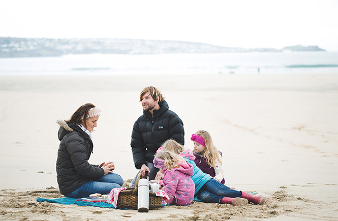 A family enjoying a wintery picnic on the beach at Hayle Towans in Cornwall