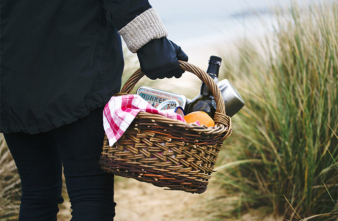 Someone carrying a picnic basket with food and wine through the dunes to Hayle Towans