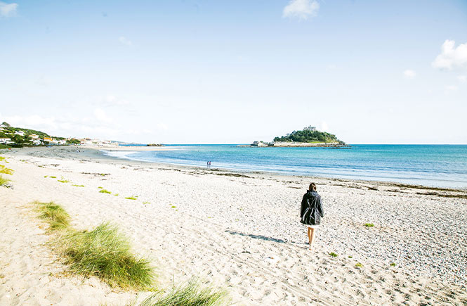 Someone walking across the sand at Marazion Beach with St Michael's Mount in the distance