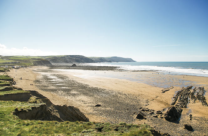 Looking across the sand and shingle beach at Black Rock Beach in Bude with dramatic cliffs in the background