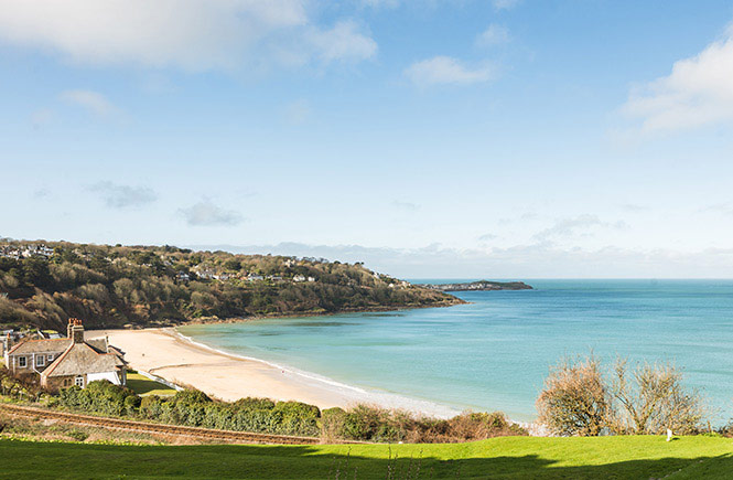 Looking over some grass at the golden sands and blue seas of Carbis Bay in Cornwall