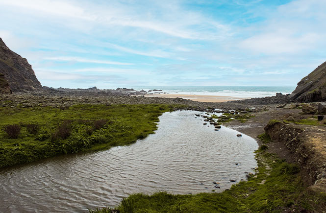 A river running down to the sand and sea at Duckpool Beach in Bude