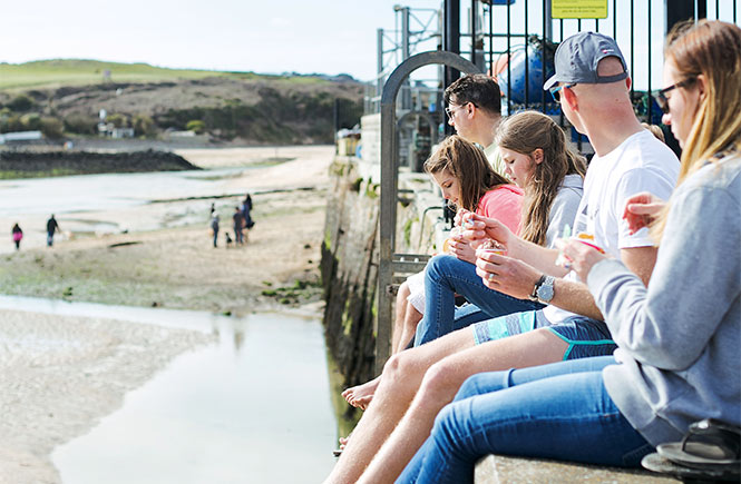 People sitting on the wall eating ice cream above Hayle beach in Cornwall