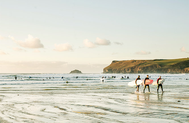 People walking across Polzeath beach with their surfboards in autumn