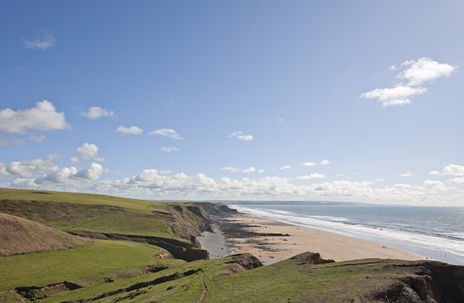 Looking across the green cliffs, golden sand beach, and blue waters at Sandymouth Beach in Bude