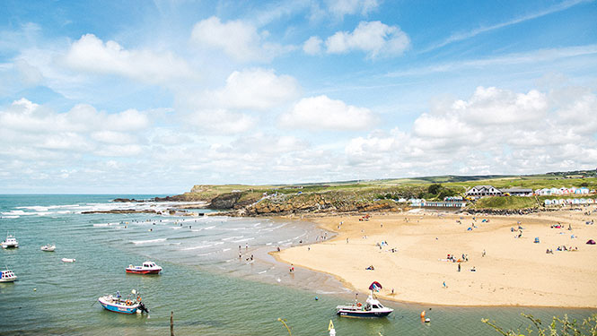 The turquoise waters and golden sands at Summerleaze Beach in Bude, with colourful beach huts on the cliffs behind