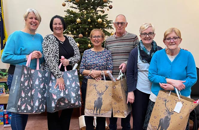 A group of six people hold Christmas bags filled with donated gifts