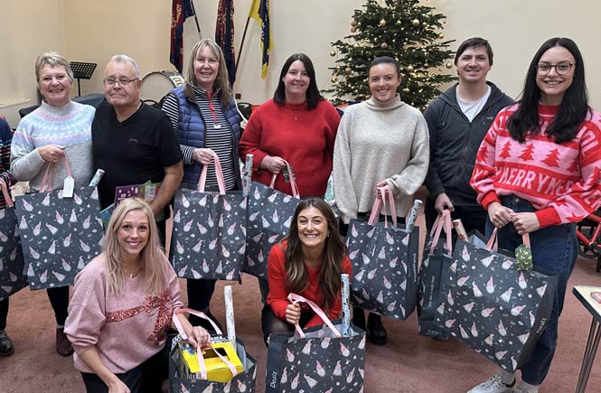 Team members stand together holding Christmas bags filled with gifts.