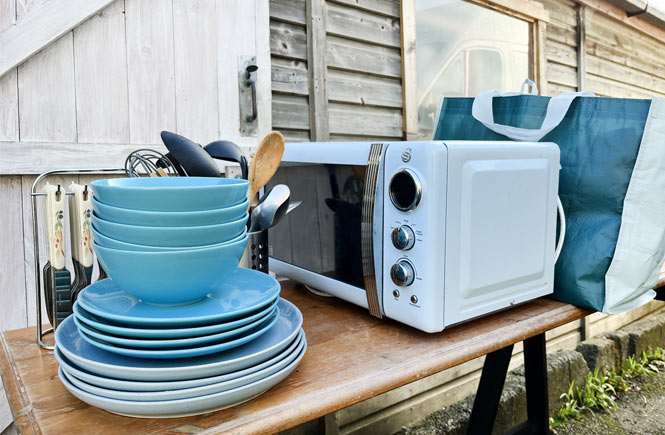 A pile of plates and a microwave are sorted on a table