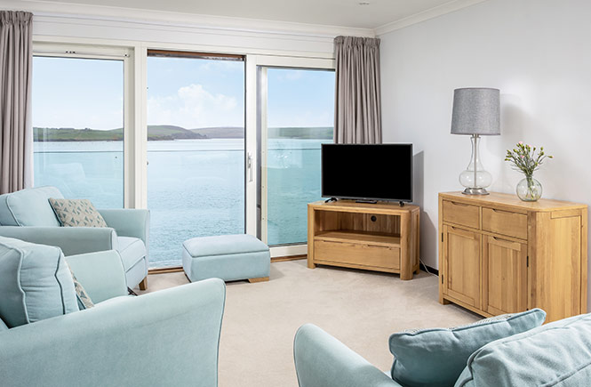 Floor to ceiling windows offer a view across the sea from the blue sofas