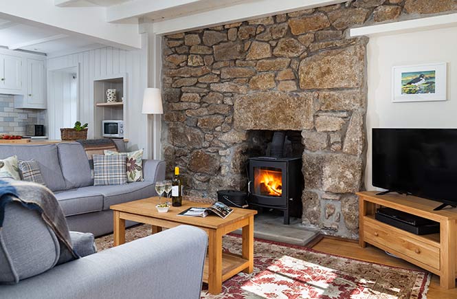 A fire is lit in the cosy sitting room of a Cornish cottage