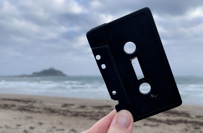 a cassette tape is help up with the beach in the background