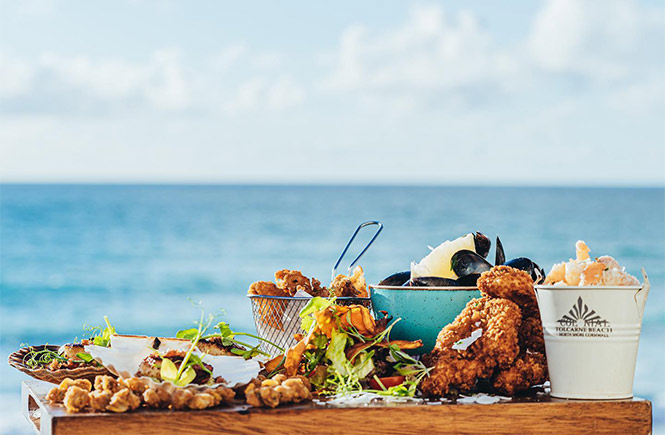 A platter of seafood with sea views behind at Colonial Beach Bar & Restaurant in Newquay