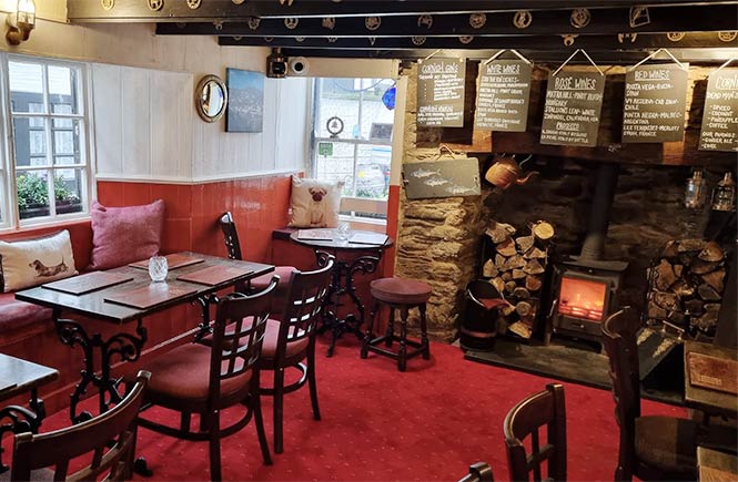 The cosy dining room with a fireplace and tables at The Three Pilchards pub in Cornwall