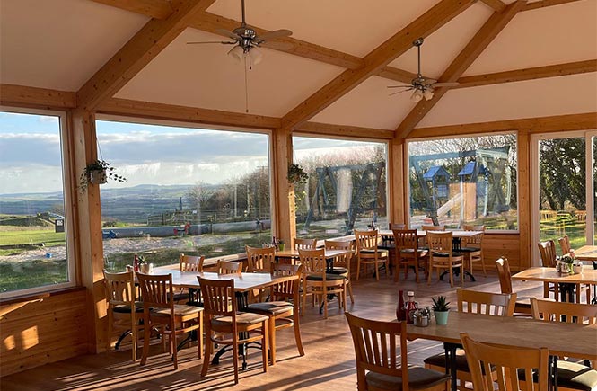 Lots of wooden tables and chairs overlooking the countryside at Trevathan Farm Shop & Restaurant